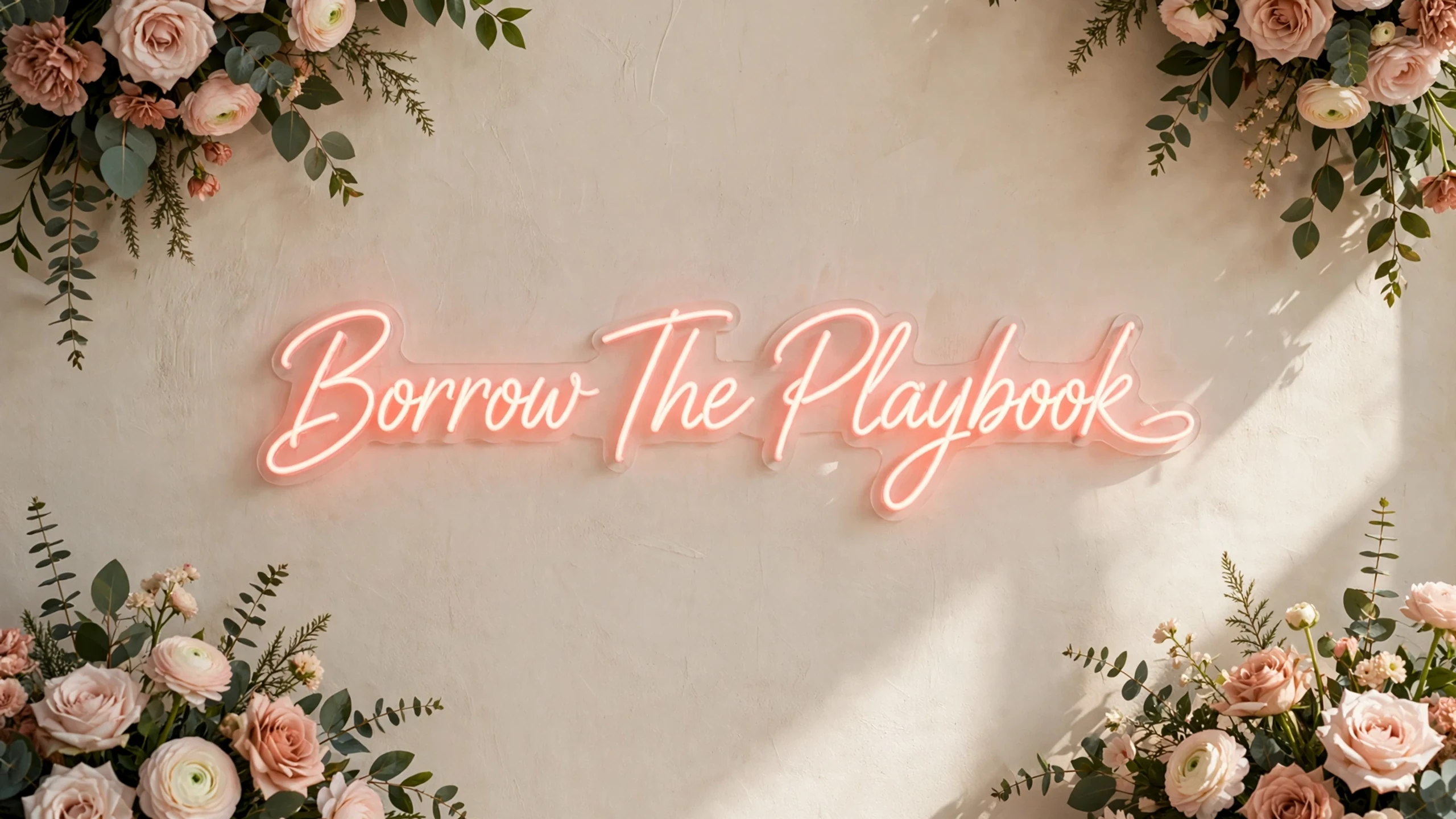 Neon script reading Borrow The Playbook framed by foliage.
