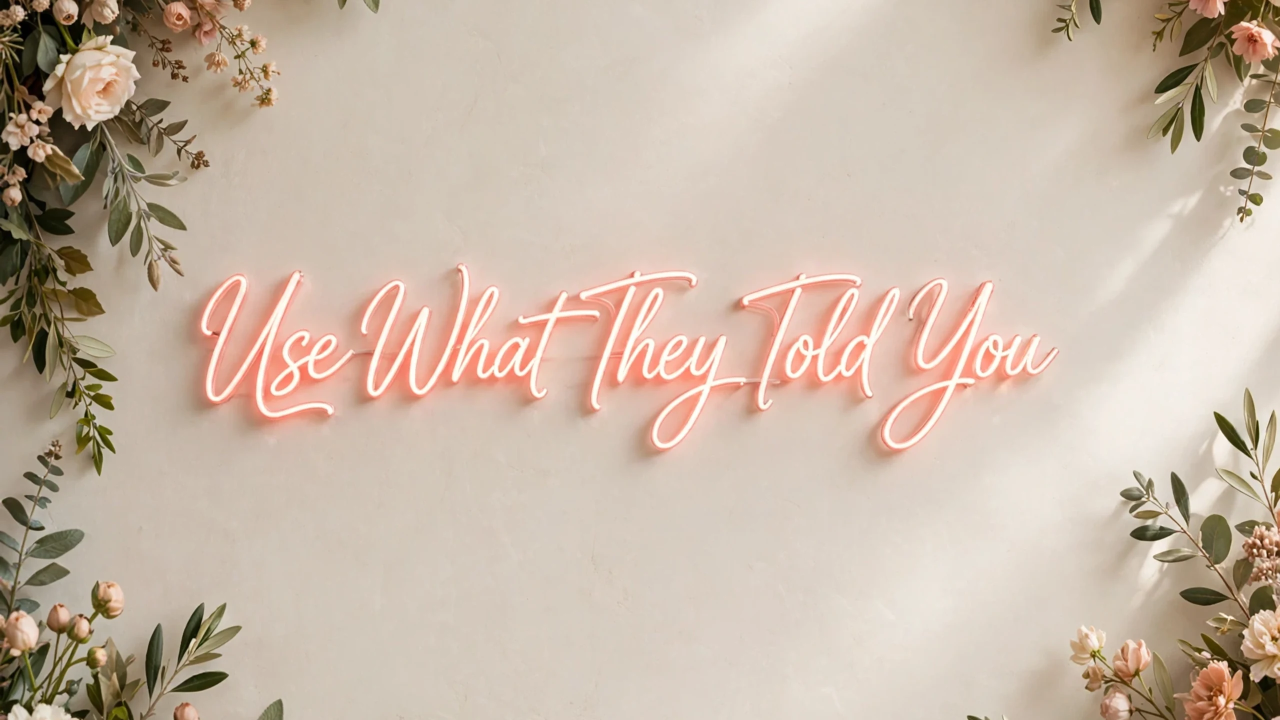 Neon script reading Use What They Told You framed by foliage.